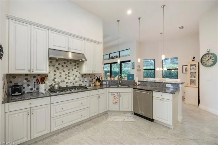 Kitchen featuring dark stone counters, hanging light fixtures, appliances with stainless steel finishes, under cabinet range hood, and tasteful backsplash