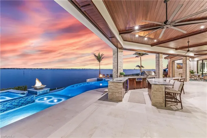 Patio terrace at dusk featuring area for grilling, a water view, an outdoor bar, and ceiling fan