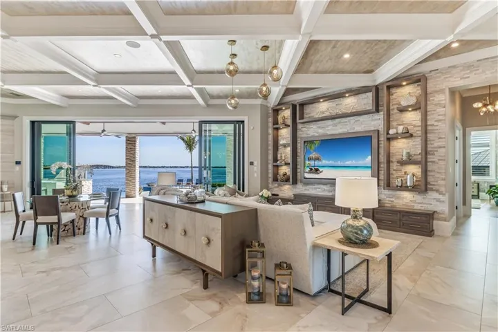 Living room featuring ceiling fan with notable chandelier, beamed ceiling, and coffered ceiling