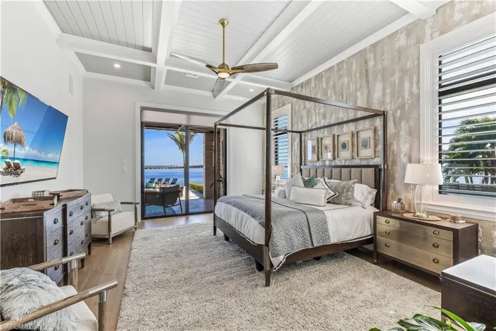 Bedroom featuring hardwood / wood-style floors, access to outside, a water view, ceiling fan, and beamed ceiling