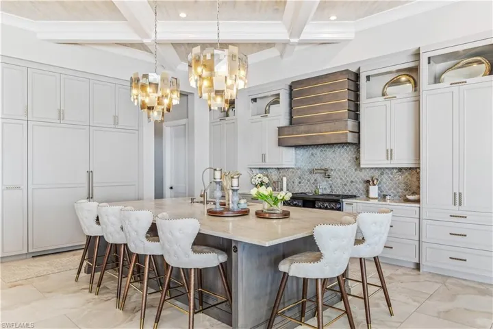 Kitchen with a large island with sink, light stone countertops, beamed ceiling, a kitchen bar, and custom range hood