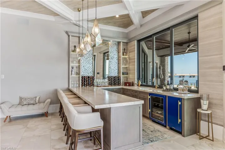 Bar with coffered ceiling, wine cooler, blue cabinets, decorative light fixtures, and a water view