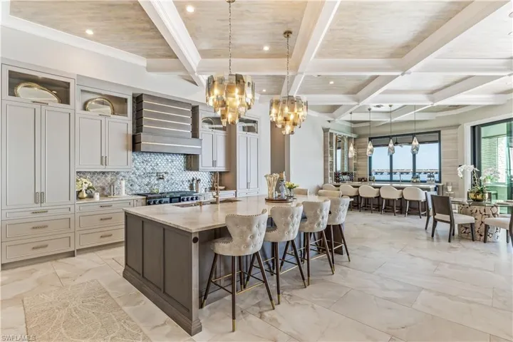 Kitchen with a kitchen bar, premium range hood, light stone counters, sink, and a large island