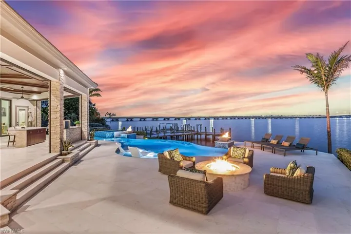 Pool at dusk featuring a fire pit, a water view, and a patio