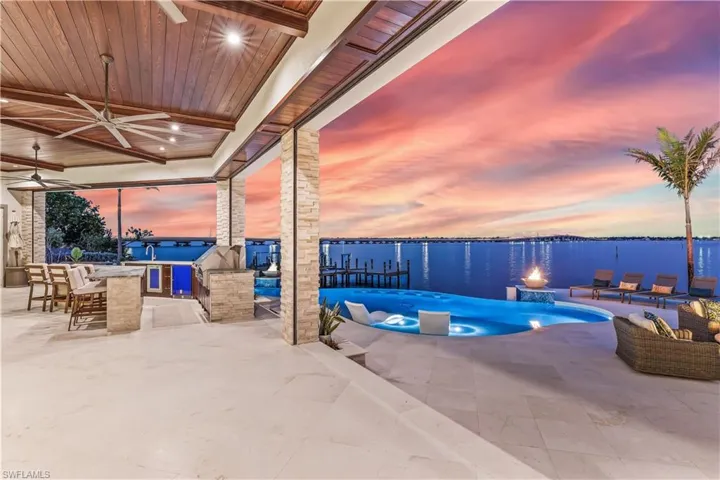 Pool at dusk featuring a water view, an outdoor bar, ceiling fan, and a patio area