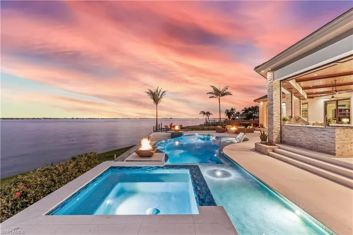 Pool at dusk featuring a patio area, an in ground hot tub, and a water view