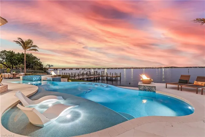 Pool at dusk featuring pool water feature, a water view, a patio area, an in ground hot tub, and a dock