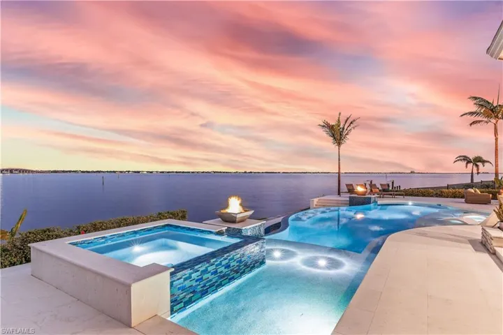 Pool at dusk with a water view and an in ground hot tub