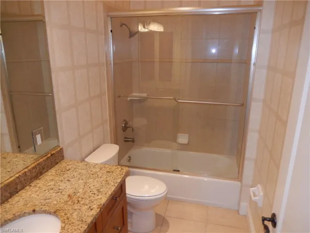 Full bath with vanity, tile patterned flooring, tile walls, and bath / shower combo with glass door