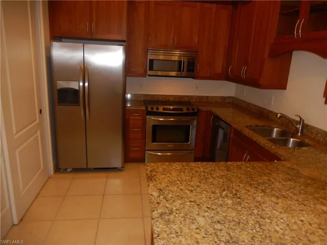 Kitchen featuring stainless steel appliances, light tile patterned flooring, light stone counters, and brown cabinetry
