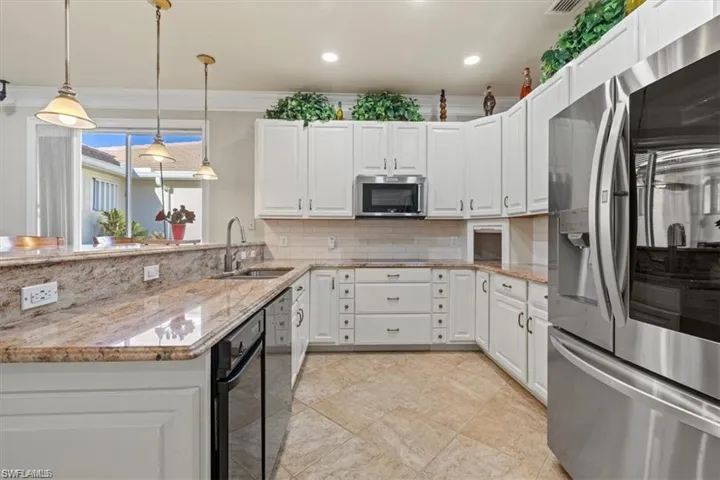 Kitchen with stainless steel appliances, a sink, decorative backsplash, white cabinets, and decorative light fixtures