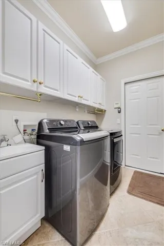 Laundry room featuring independent washer and dryer, ornamental molding, cabinet space, and light tile patterned floors