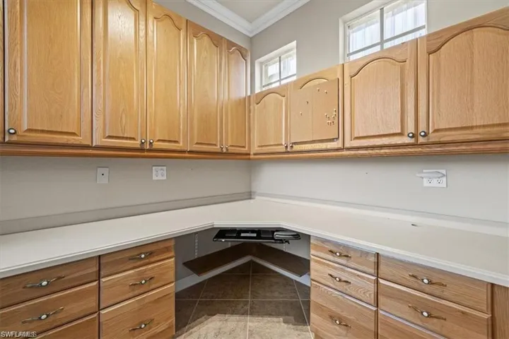 Unfurnished office with ornamental molding, built in desk, and tile patterned floors