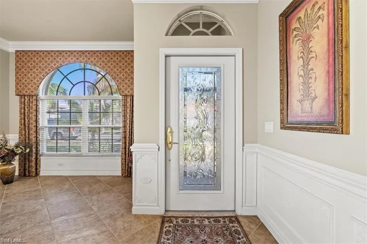 Foyer entrance with ornamental molding, wainscoting, and light tile patterned floors