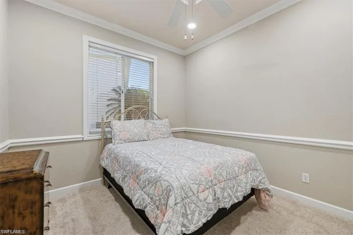 Carpeted bedroom featuring baseboards, crown molding, and a ceiling fan