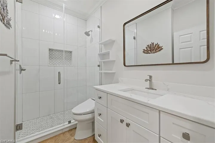 Bathroom with vanity, toilet, a stall shower, crown molding, and tile patterned floors