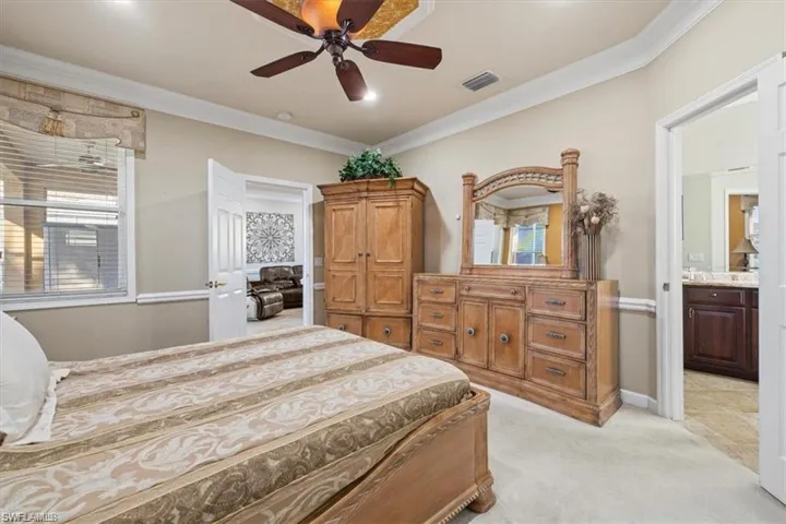 Bedroom with light colored carpet, ornamental molding, a ceiling fan, and ensuite bathroom