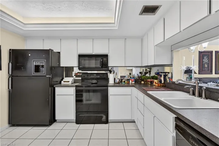 Kitchen with black appliances, white cabinets, dark countertops, and a tray ceiling