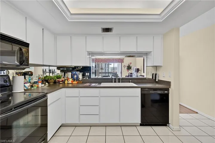 Kitchen with black appliances, white cabinetry, dark countertops, and light tile patterned flooring