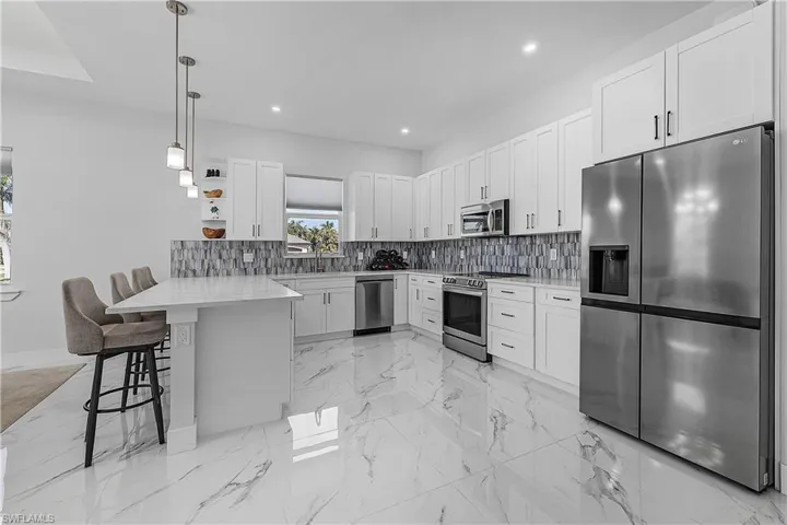 Kitchen featuring a kitchen bar, white cabinetry, appliances with stainless steel finishes, kitchen peninsula, and pendant lighting