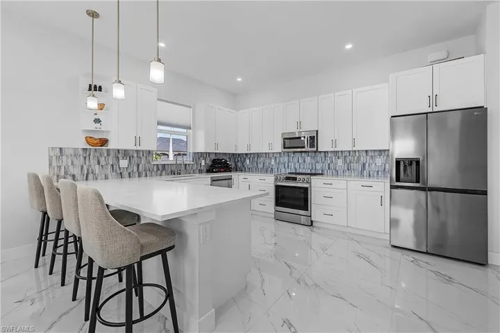 Kitchen featuring a breakfast bar area, white cabinetry, hanging light fixtures, and stainless steel appliances