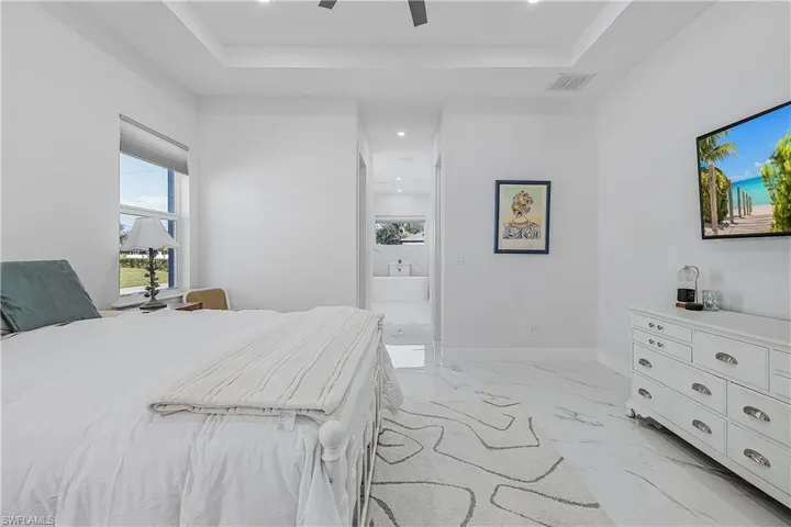 Bedroom with a tray ceiling, ceiling fan, and ensuite bathroom
