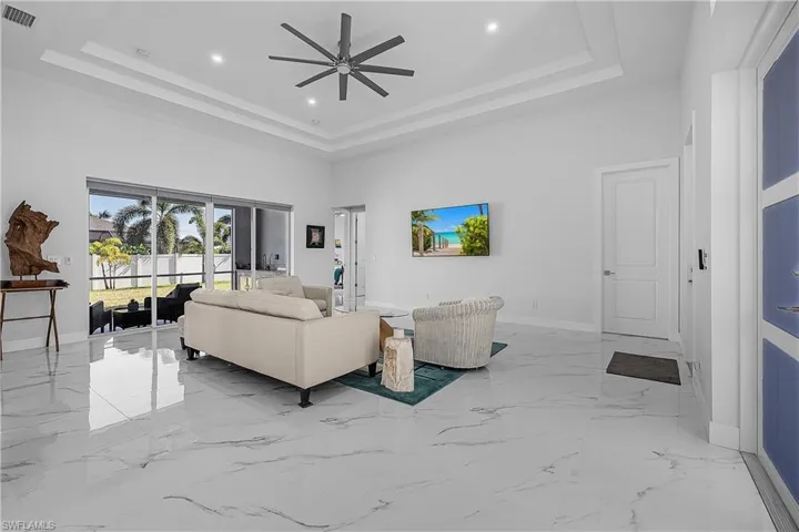Living room featuring a ceiling fan, a tray ceiling, and sliders to the outdoor space