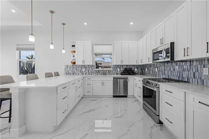 Kitchen with sink, appliances with stainless steel finishes, hanging light fixtures, white cabinets, and a kitchen bar
