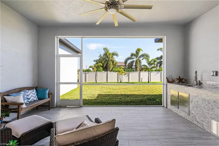 Covered and screened lanai space featuring ceiling fan, sink, and a view of the backyard
