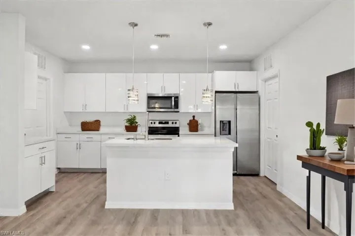Kitchen with pendant lighting, light hardwood / wood-style flooring, appliances with stainless steel finishes, white cabinetry, and a center island with sink
