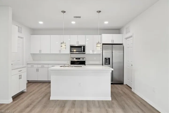 Kitchen with pendant lighting, a kitchen island with sink, light hardwood / wood-style flooring, appliances with stainless steel finishes, and white cabinetry