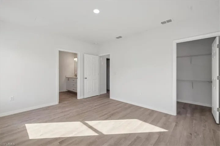 Unfurnished bedroom featuring light hardwood / wood-style floors, a walk in closet, connected bathroom, and a closet