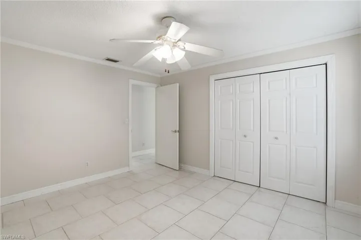 Spacious room featuring neutral wall tones, large format tile flooring, crown molding, and a ceiling fan with integrated lighting