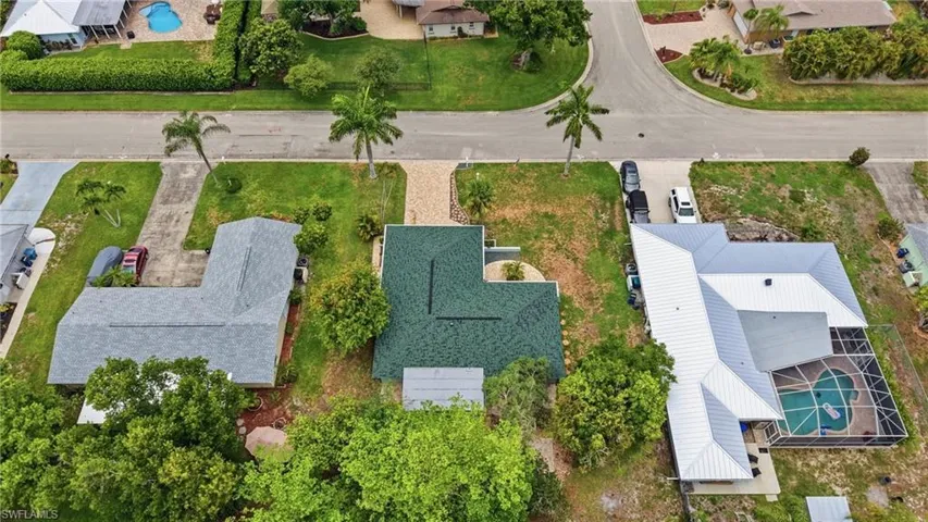 Single-story residence with a green shingle roof, complemented by a paved driveway and mature palm trees