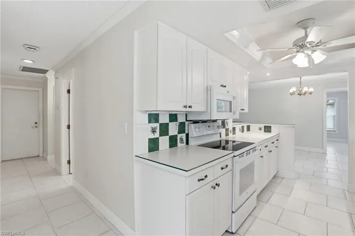 Kitchen featuring white cabinetry, a built-in microwave, an electric range, and a green and white checkerboard backsplash