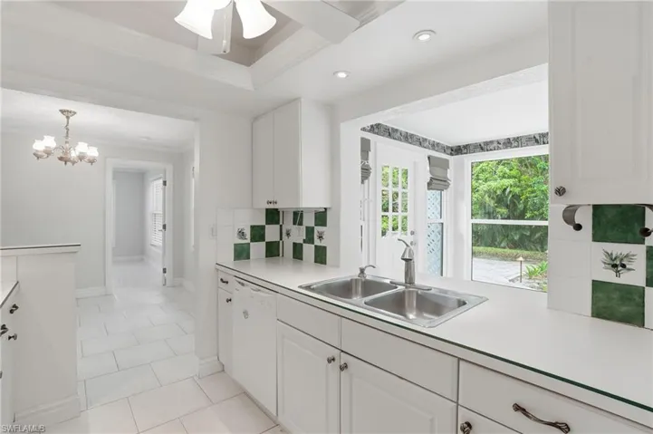 Kitchen featuring a stainless steel double sink, white cabinetry, integrated dishwasher, and a green and white tiled backsplash