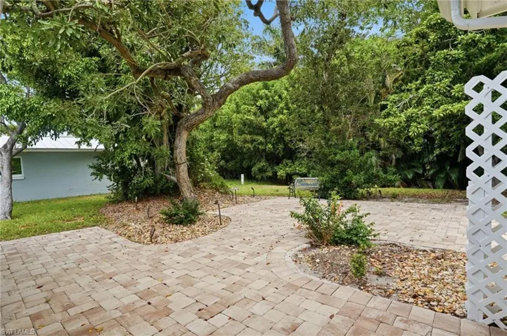 Expansive paver patio with integrated landscape beds, mature trees, and lush surrounding foliage
