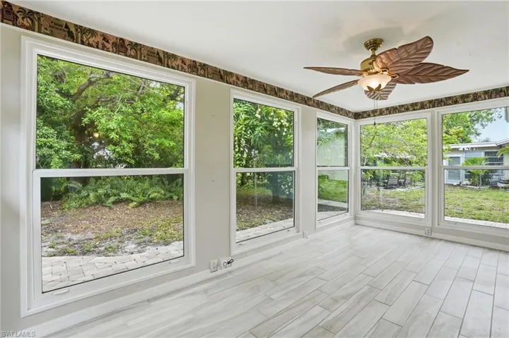Room featuring multiple large windows, wood-finish flooring, and a ceiling fan with leaf-shaped blades