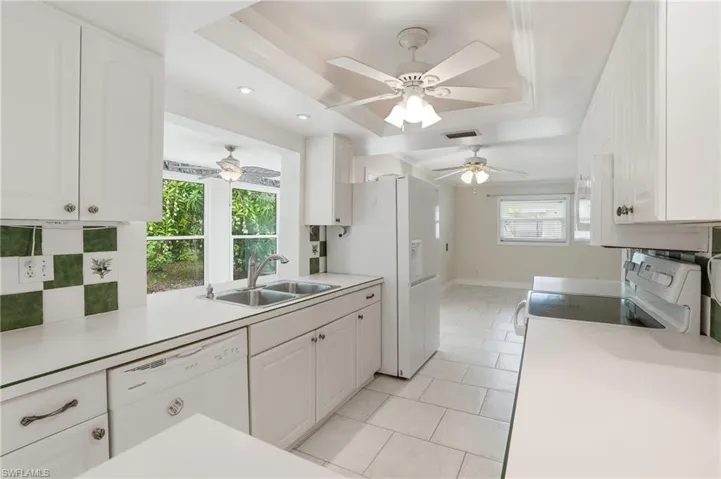 Bright kitchen featuring white cabinetry, a dual basin stainless steel sink, and a white appliance suite