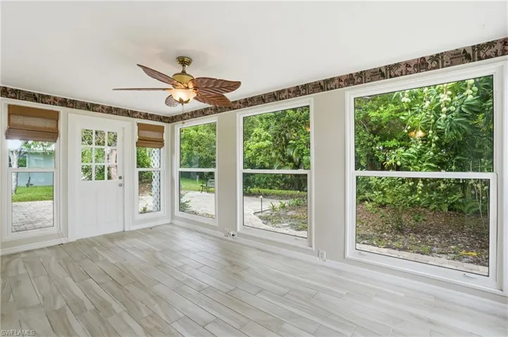 Sun-filled room featuring extensive window-paneled walls, wood-finish flooring, and a decorative ceiling fan