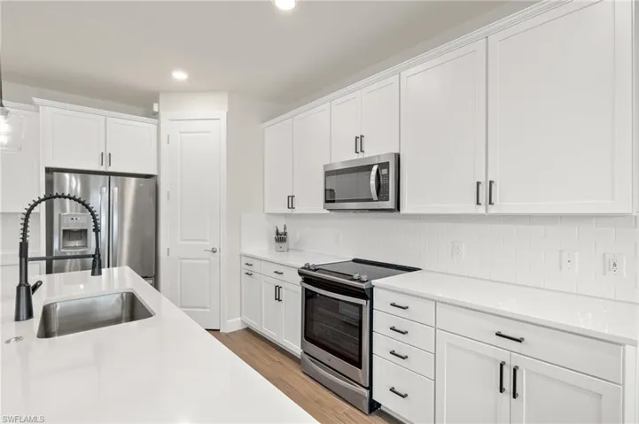 Kitchen with stainless steel appliances, white cabinetry, light hardwood / wood-style floors, and backsplash