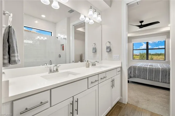 Bathroom with tiled shower, dual vanity, and ceiling fan