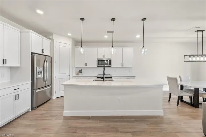 Kitchen featuring a center island with sink, light hardwood / wood-style flooring, appliances with stainless steel finishes, white cabinets, and decorative light fixtures