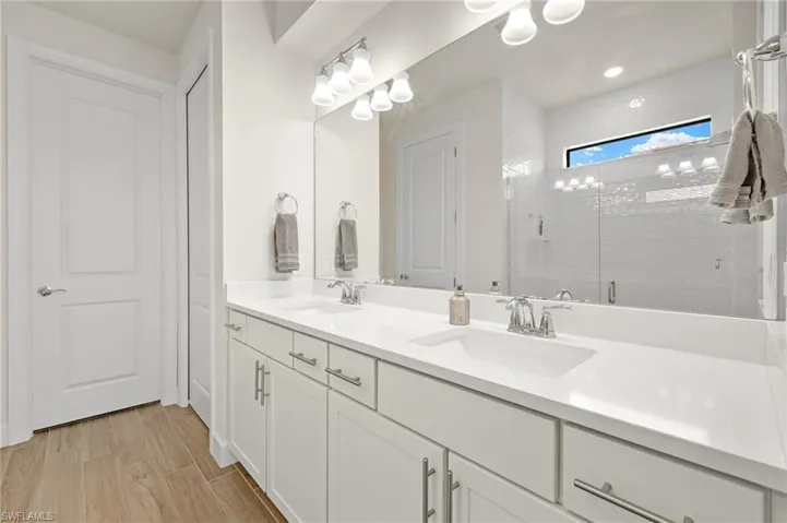 Bathroom featuring tiled shower, hardwood / wood-style flooring, and dual bowl vanity