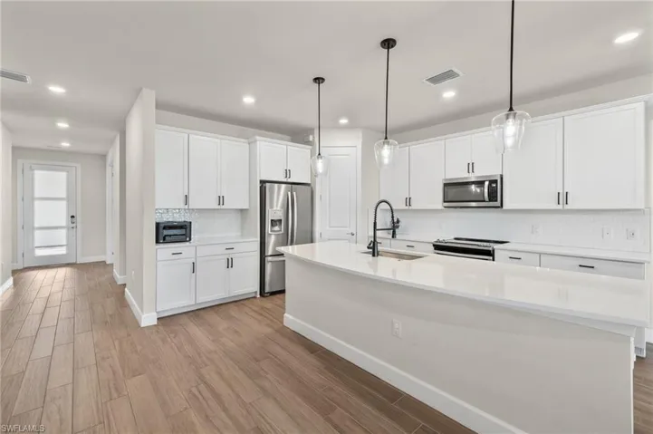 Kitchen with light hardwood / wood-style floors, tasteful backsplash, a kitchen island with sink, appliances with stainless steel finishes, and sink
