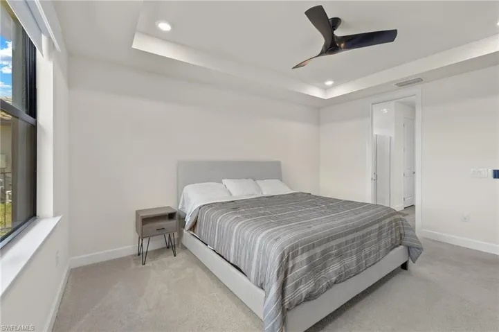 Carpeted bedroom with ceiling fan and a tray ceiling