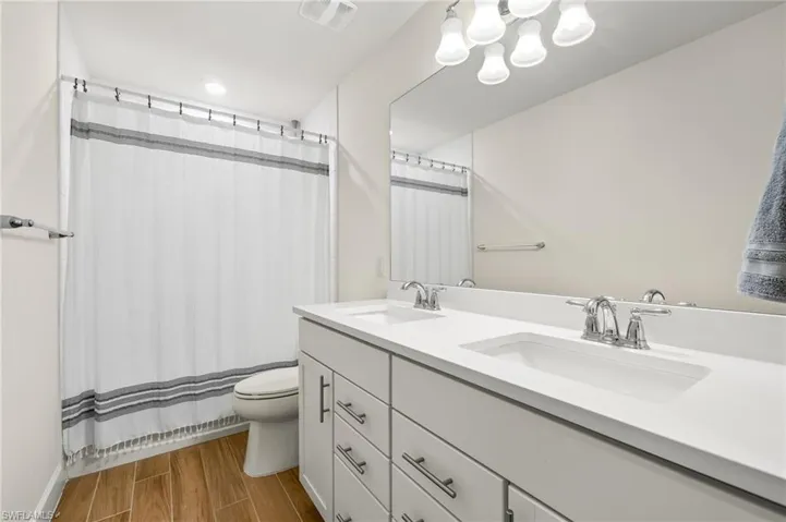 Bathroom featuring hardwood / wood-style floors, oversized vanity, dual sinks, and toilet