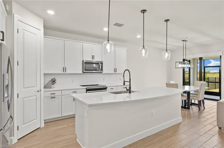 Kitchen with white cabinetry, hanging light fixtures, appliances with stainless steel finishes, sink, and tasteful backsplash