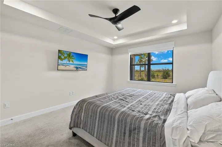 Carpeted bedroom featuring ceiling fan and a raised ceiling