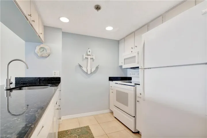 Kitchen with white appliances, light tile patterned floors, white cabinetry, and dark stone counters